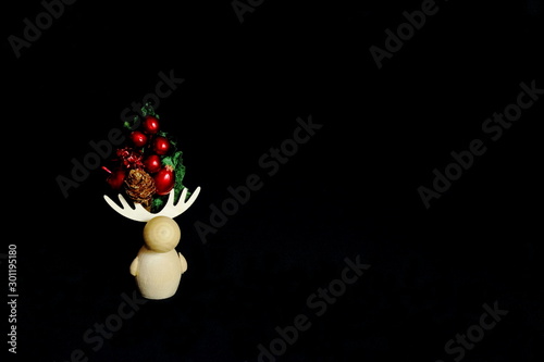 Wooden figure of deer decorated with bright Christmas bouquet on black background. Concept Christmas, holiday, New Year, congratulatory background. Minimal style.