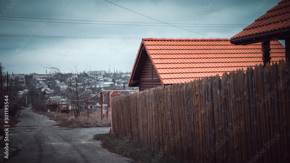 Rural street. Fence made of sharp wooden stakes. House with a red tiled roof Rural street. Fence made of sharp wooden stakes. House with a red tiled roof