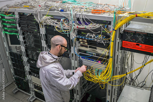 A technician connects Internet backbone wires to the server room. The specialist works near the server racks of the datacenter. A man maintains computer equipment. View from above