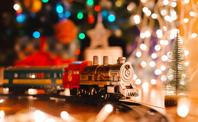 toy vintage steam locomotive on the floor under a decorated Christmas tree on a background of bokeh lights garland.