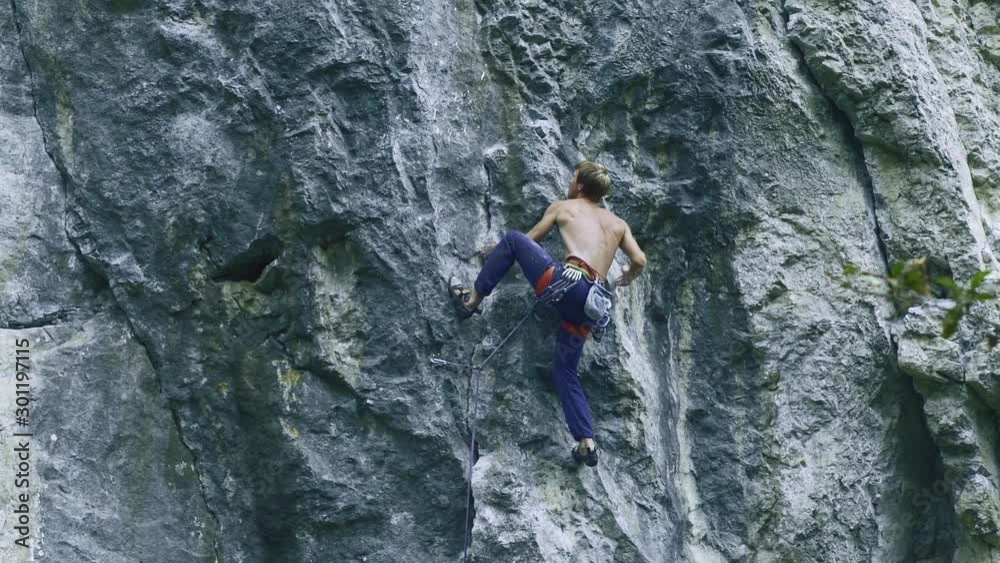 back view strong muscular man rock climber climbing on sport route outdoors on a vertical cliff, making hard wide move and gripping hold. 120 fps slow motion back view strong muscular man rock climber climbing on sport route outdoors on a vertical cliff, making hard wide move and gripping hold. 120 fps slow motion