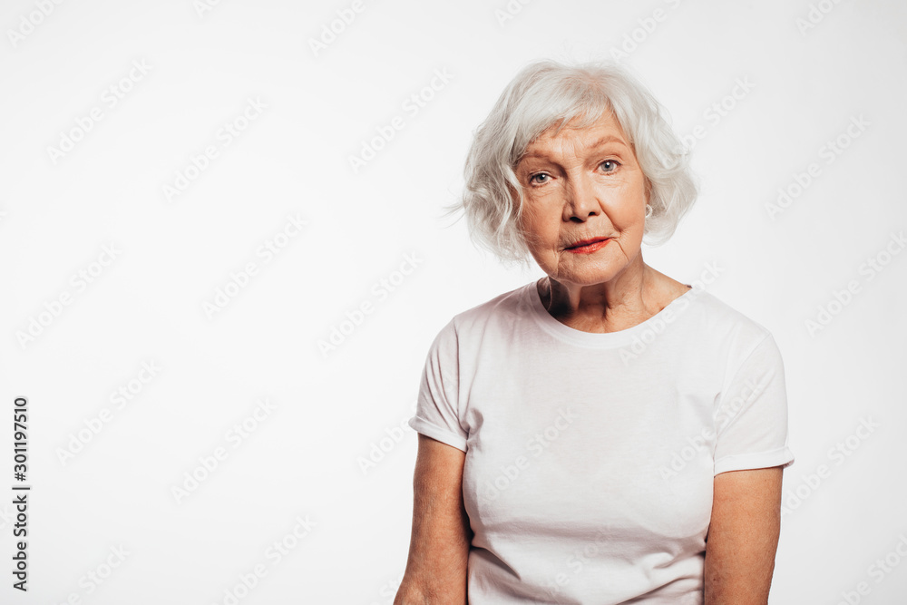 Old woman with white hair and wrinkles on face. Sit alone and pose on camera.Look straight without smile. Wear white shirt. Isolated over white background. Old woman with white hair and wrinkles on face. Sit alone and pose on camera.Look straight without smile. Wear white shirt. Isolated over white background.