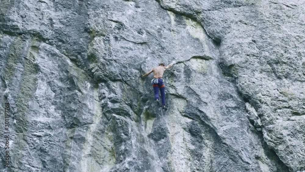 back view strong muscular man rock climber climbing on sport route outdoors on a vertical cliff, attaching quickdraw and clipping rope. 120 fps slow motion back view strong muscular man rock climber climbing on sport route outdoors on a vertical cliff, attaching quickdraw and clipping rope. 120 fps slow motion