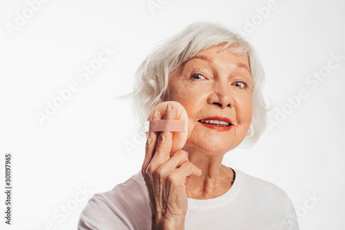 Nice attractive old woman take care about her skin with sponge. Beauty treatment at home. Anti age procedure. Wan to stay young forever. Isolated over white background.