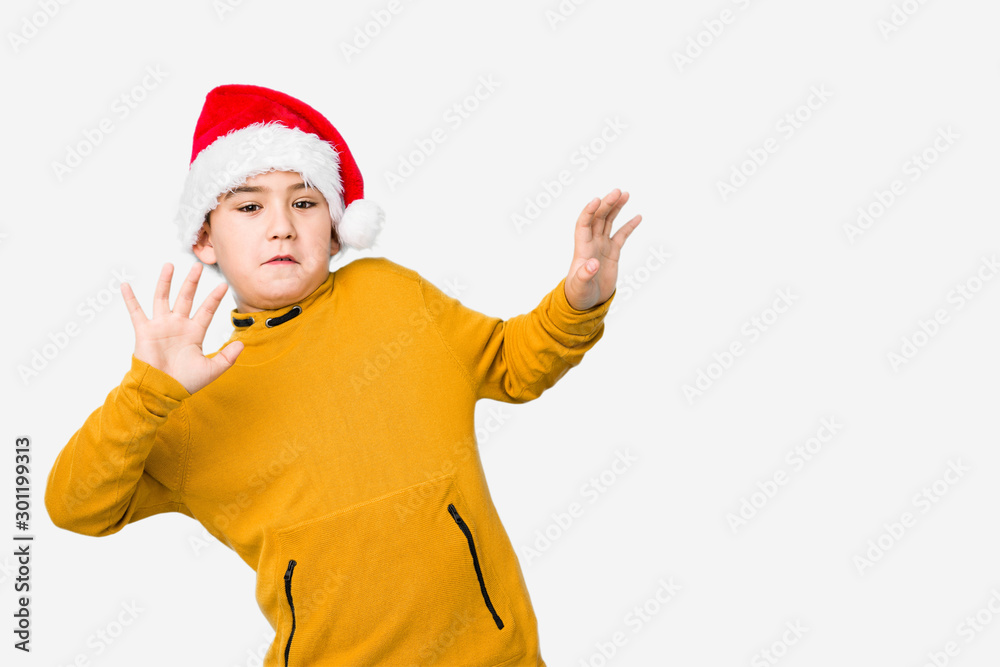 Little boy celebrating christmas day wearing a santa hat isolated being shocked due to an imminent danger Little boy celebrating christmas day wearing a santa hat isolated being shocked due to an imminent danger