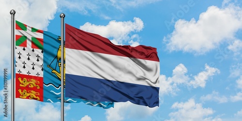 Saint Pierre And Miquelon and Netherlands flag waving in the wind against white cloudy blue sky together. Diplomacy concept, international relations.