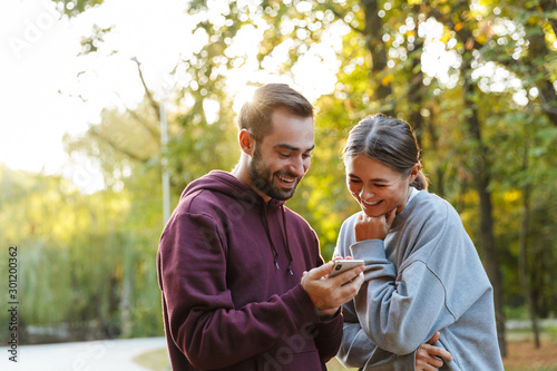 Photo of beautiful pleased couple using cellphone and laughing