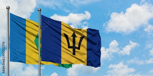 Saint Vincent And The Grenadines and Barbados flag waving in the wind against white cloudy blue sky together. Diplomacy concept, international relations.