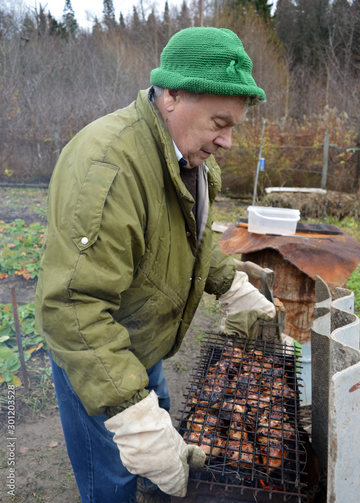 An elderly man cooks food over a fire in the garden in autumn and laughs An elderly man cooks food over a fire in the garden in autumn and laughs