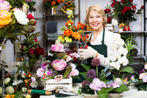 Florist in apron holding scissors and fixing flowers