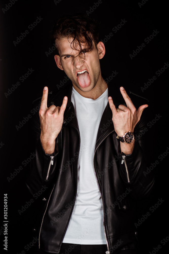 brutal man sticking out tongue and showing rock sign isolated on black