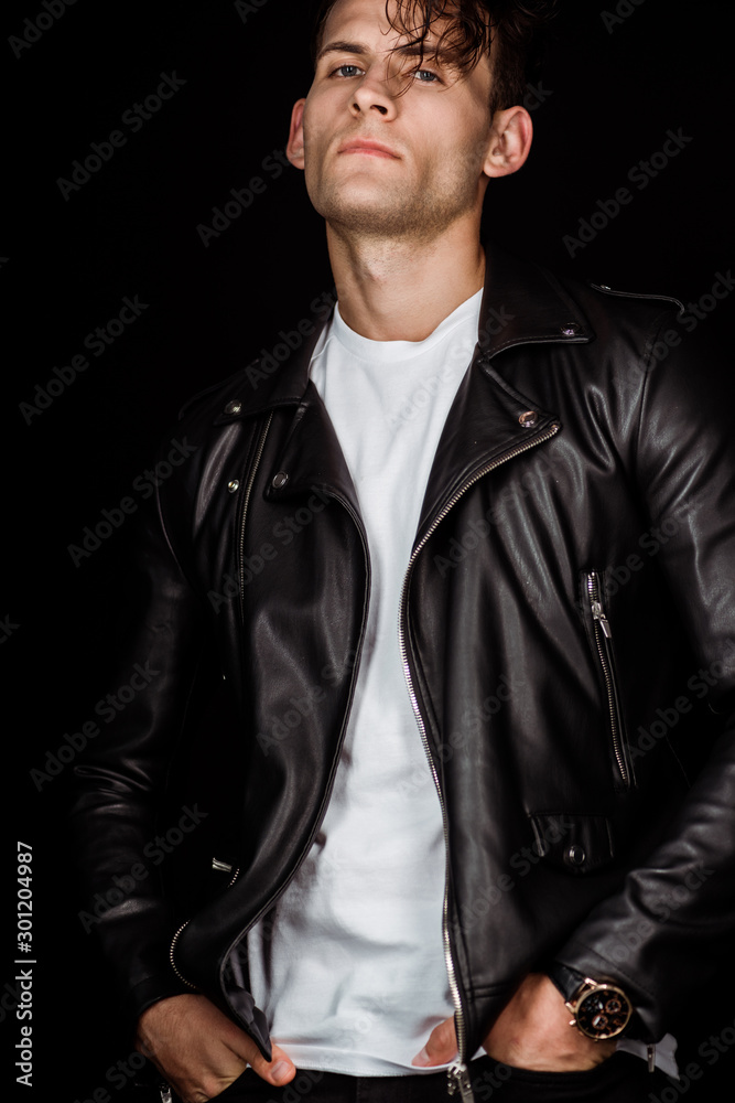 stylish man in leather jacket standing with hands in pockets isolated on black