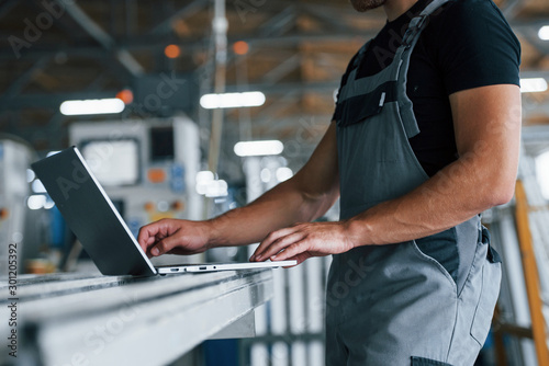 Modern laptop. Typing on keyboard. Industrial worker indoors in factory. Young technician with orange hard hat © standret