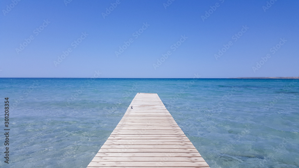 Wooden pier with blue sea and blue sky on background. Wooden bridge on the beach to the sea in the blue sky. Wooden bridge on the beach and blue sky in summer.