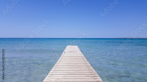 Wooden pier with blue sea and blue sky on background. Wooden bridge on the beach to the sea in the blue sky. Wooden bridge on the beach and blue sky in summer.