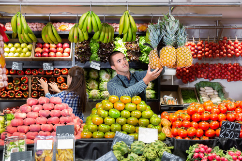 Friendly man and woman laying out vegetables and fruits in shop © JackF