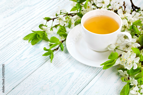 Green tea in a ceramic cup with branches of blossoming apple tree on a white wooden background.