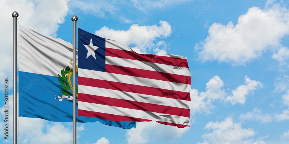 San Marino and Liberia flag waving in the wind against white cloudy blue sky together. Diplomacy concept, international relations.