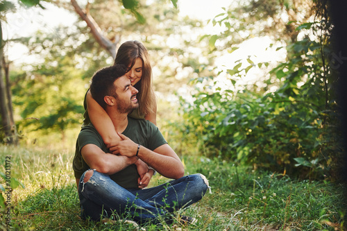 Sitting and embracing. Beautiful young couple have a good time in the forest at daytime