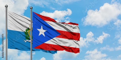 San Marino and Puerto Rico flag waving in the wind against white cloudy blue sky together. Diplomacy concept, international relations.