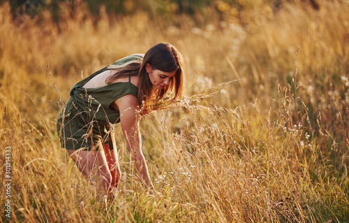 Beautful girl walks through the field with high grass and collecting flowers. Amazing sunlight