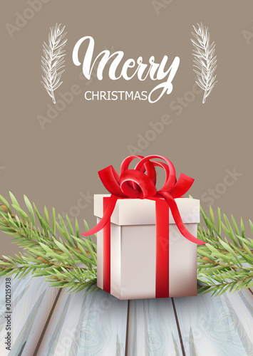 Merry christmas gift box with red ribbon and fir tree leaves. Wooden table. H...