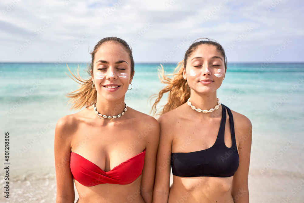 Two young women standing on the beach with closed eyes Two young women standing on the beach with closed eyes