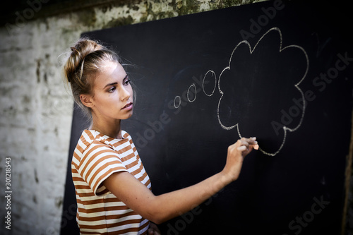Pensive young woman drawing a thought bubble on a blackboard