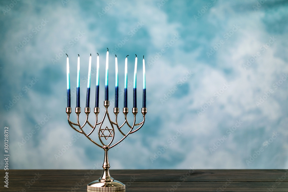 A silver menorah for the Jewish holiday Hanukkah with burning glowing eight candles not lit on a blue background with copy space A silver menorah for the Jewish holiday Hanukkah with burning glowing eight candles not lit on a blue background with copy space