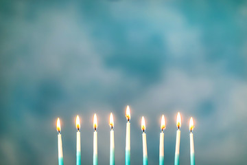 A silver menorah for the Jewish holiday Hanukkah with burning glowing eight candles on fire lit up on a blue background with copy space