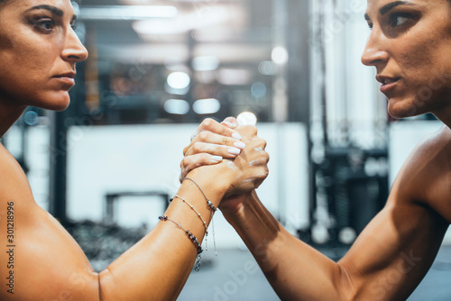 Female twins in good shape doing arm wrestling challenge in a gym photo