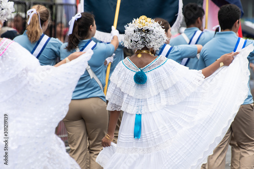 Unidentifiable woman wearing traditional white Panamanian dress and other people in the street during Panama National Day parade celebrating the separation of Panama from Colombia. Selective focus.