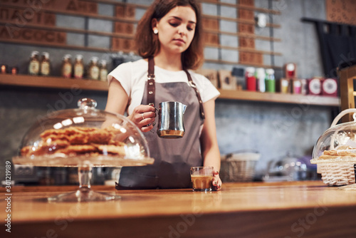 Pouring fresh coffee. Young female worker indoors. Conception of business and service