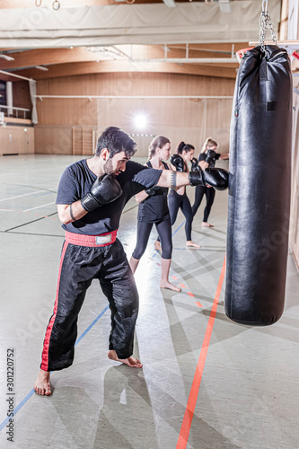 Coach and female, boxers practicing at punchbag in sports hall photo