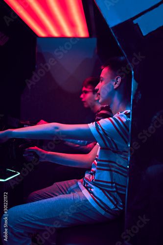 Teenage friends playing with a driving simulator in an amusement arcade