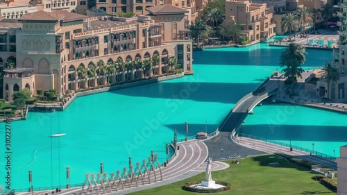 Aerial close up view of the bridge over man-made lake and some people walking in park with hand monument morning timelapse in Dubai downtown, United Arab Emirates. photo