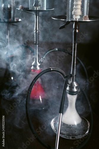 Three modern hookahs isolated on black background with clouds of smoke © ANR Production