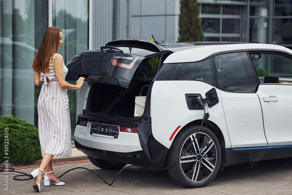 Woman on the electric cars charge station at daytime. Brand new vehicle Woman on the electric cars charge station at daytime. Brand new vehicle