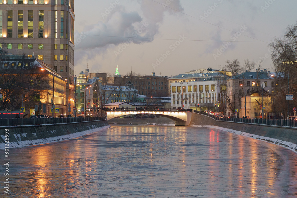 Winter coming into the city Moscow. Water in the river had been covered by ice. Buildings and city lights are reflected in the cold water and on white, gray ice floes. Suitable for greeting cards