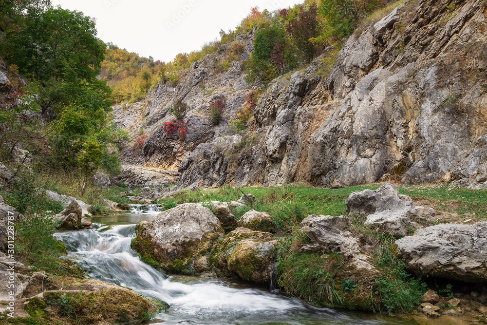 Low angle, long exposure shot of curvy mountain creek cascading through the rocky canyon and colorful, sunlit, autumn colored trees Low angle, long exposure shot of curvy mountain creek cascading through the rocky canyon and colorful, sunlit, autumn colored trees