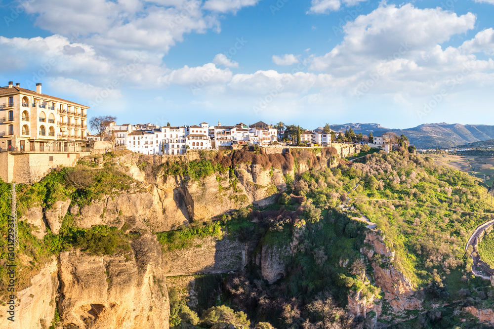 Ronda, Spain: Landscape of white houses on the green edges of steep cliffs with mountains in the background.