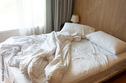 Messy bed. Couple pillows with white blanket on unmade  bed.