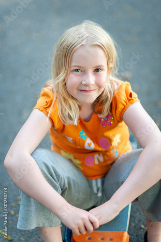 Pretty blonde girl smiling and sitting on a skateboard while making eye contact photo