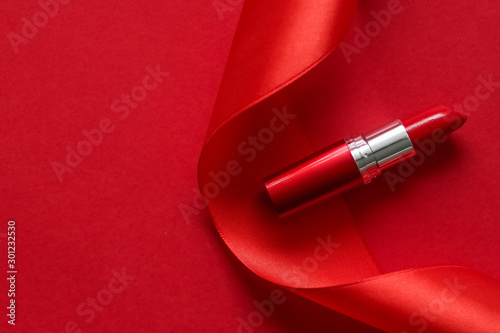 Obraz na plátne Luxury lipstick and silk ribbon on red holiday background, make-up and cosmetics