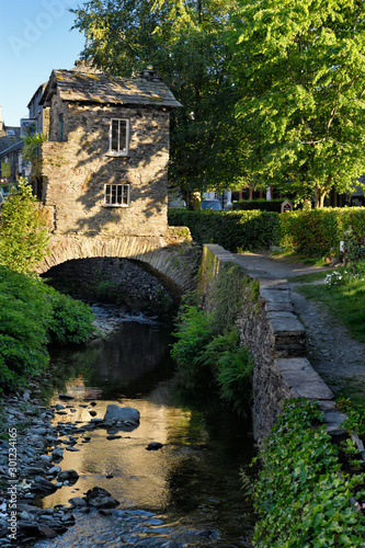 Bridge House on bridge over Stock Beck river with reflection of evening sunlight in Ambleside Lake District England