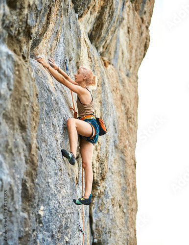 side view of young athletic woman rock climber climbing on the cliff. a woman climbs on a vertical rock wall on white background. Conquering, overcoming and active lifestyle concept.