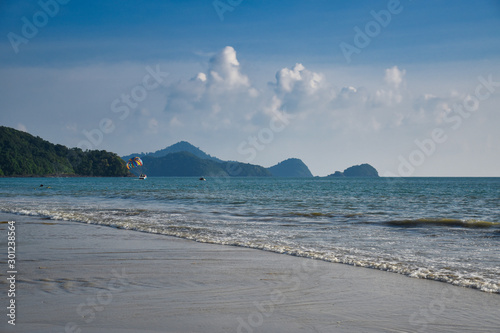 Waves of the azure Andaman sea under the blue sky reaching the shores of the sandy beautiful exotic and stunning Cenang beach in Langkawi island