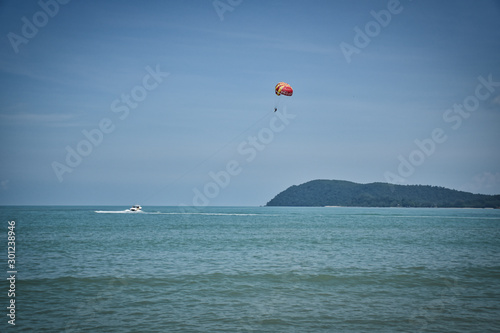 Parasailing on the waves of the azure Andaman sea under the blue sky near the shores of the sandy beautiful exotic and stunning Cenang beach in Langkawi island,