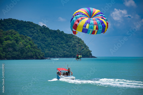 Parasailing on the waves of the azure Andaman sea under the blue sky near the shores of the sandy beautiful exotic and stunning Cenang beach in Langkawi island,