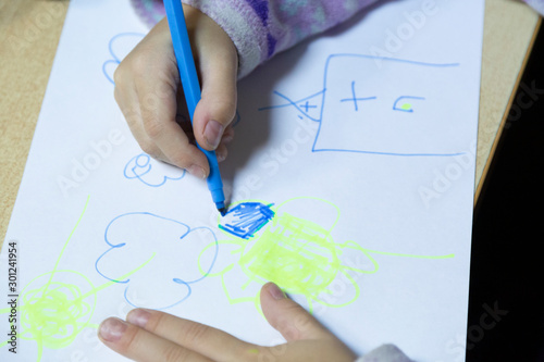 The child draws a felt-tip pen on a sheet of white paper.